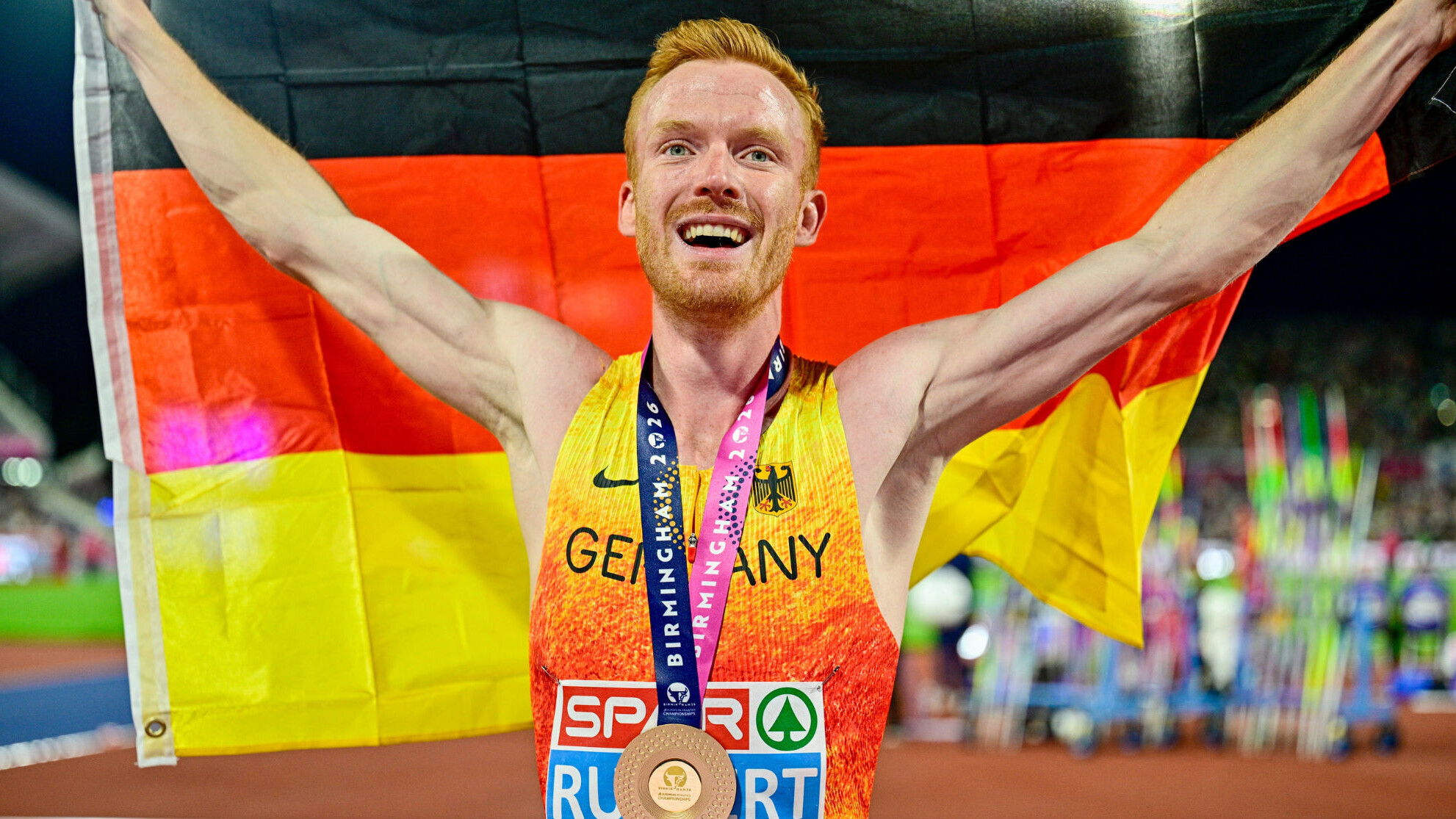 Der deutsche Hindernislaufer hält eine Deutschlandfahne in die Höhe und hat dabei eine Goldmedaille um den Hals.