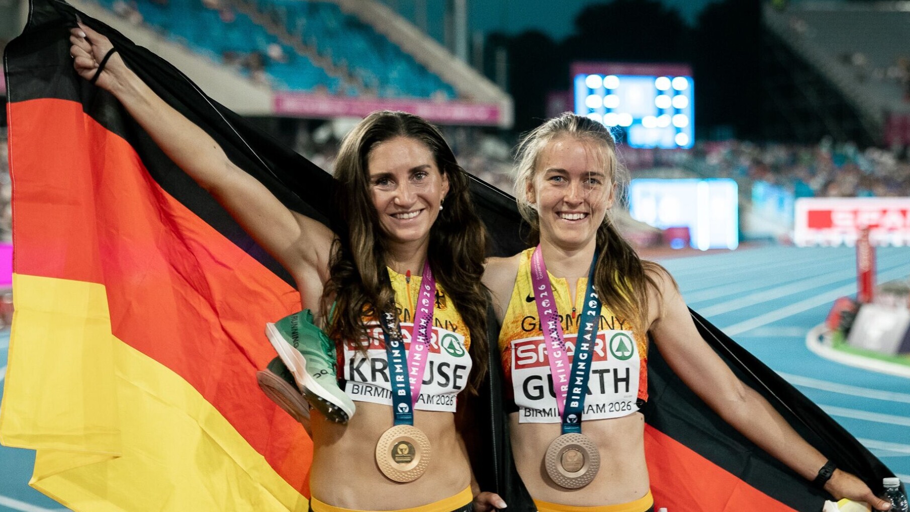 Die deutschen Hindernisläuferinnen Gesa Krause und Olivia Gürth jubeln mit der Deutschlandfahne um den Schultern und Medaillen um den Hals.