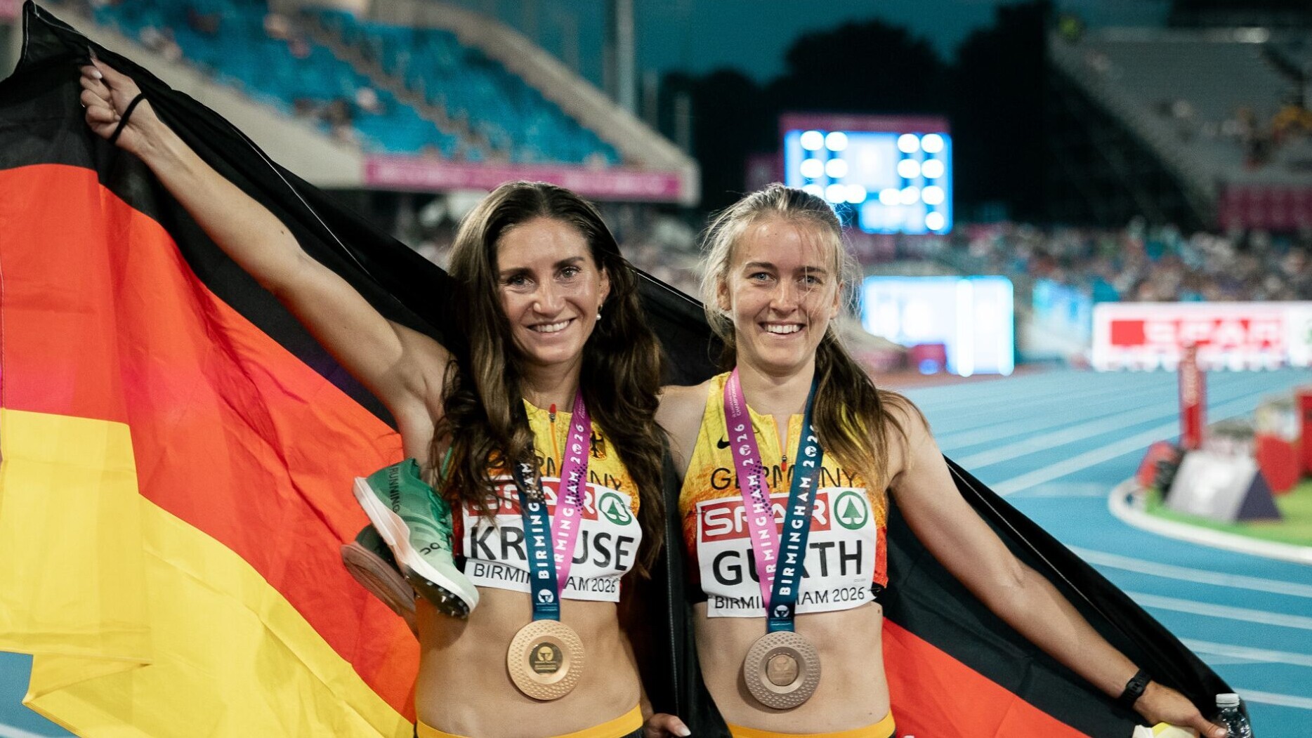 Die deutschen Hindernisläuferinnen Gesa Krause und Olivia Gürth jubeln mit der Deutschlandfahne um den Schultern und Medaillen um den Hals.