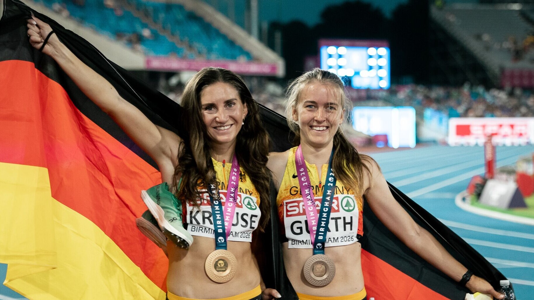 Die deutschen Hindernisläuferinnen Gesa Krause und Olivia Gürth jubeln mit der Deutschlandfahne um den Schultern und Medaillen um den Hals.