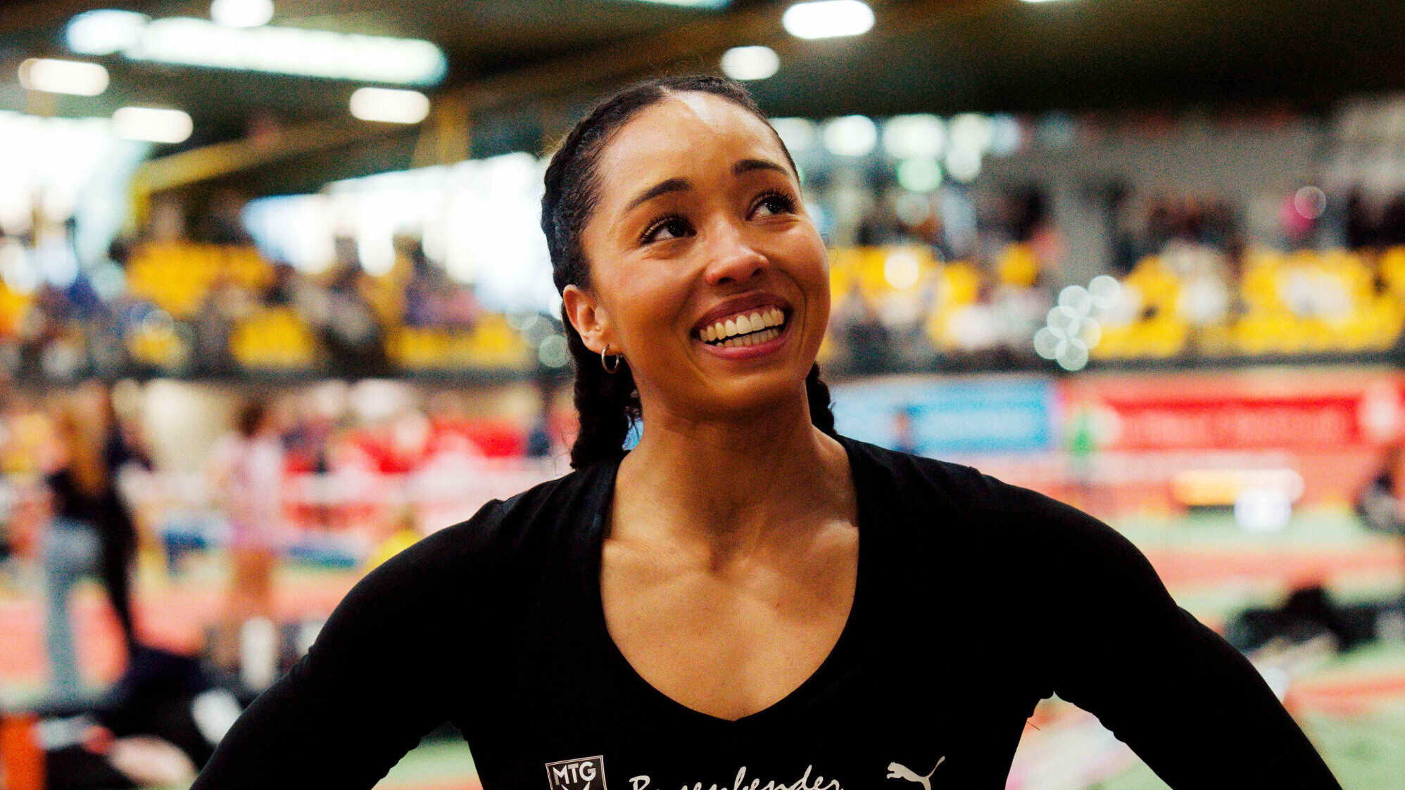 Die deutsche Stabhochspringerin Jacqueline Otchere steht lächelnd in einer Leichtathletikhalle.