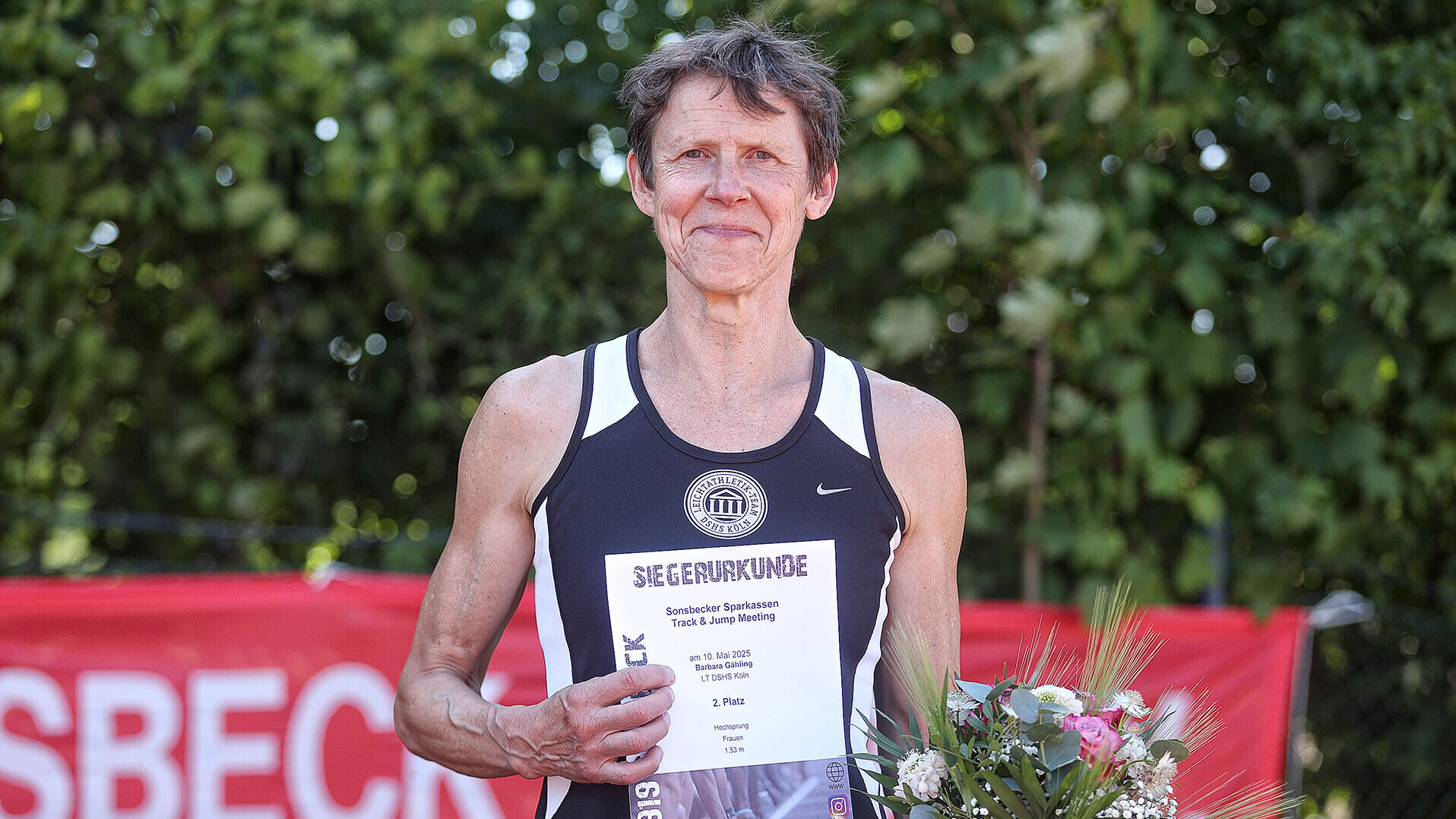 Porträt von Masters-Athletin Barbara Gähling im Vereinstrikot mit Urkunde und Blumen in der Hand