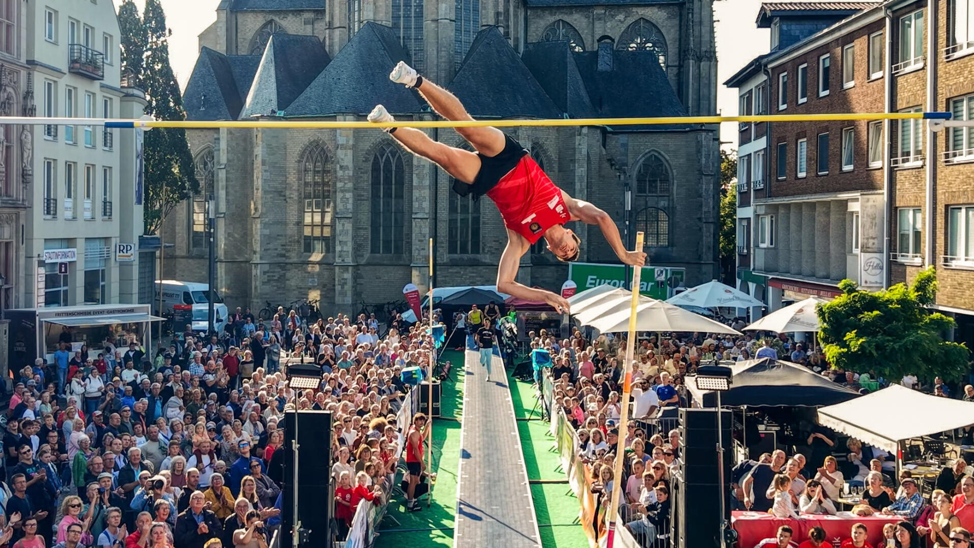 Ein Stabhochspringer fliegt vor der Wesler Dom über die Latte.