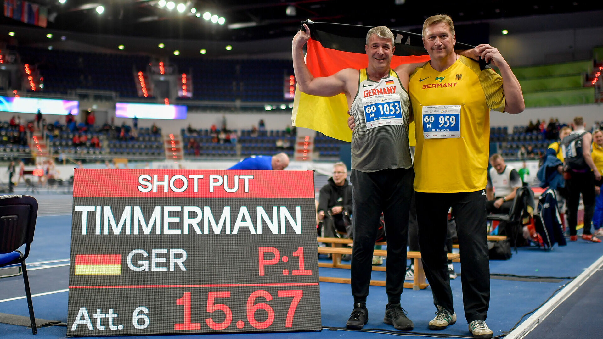 Leif Timmermann und Enrico Pyritz posieren mit Deutschlandfahne neben einer Anzeigetafel mit Aufschrift "Timmermann 15,67"