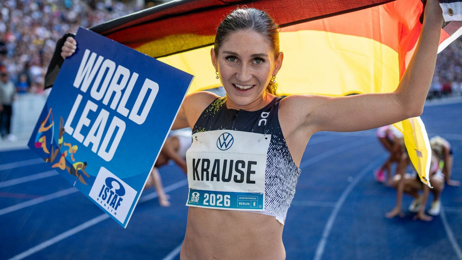 Die deutsche Läuferin Gesa Krause jubelt mit einer Deutschlandfahne um den Schultern und einem Schild "World Lead" in der Hand.
