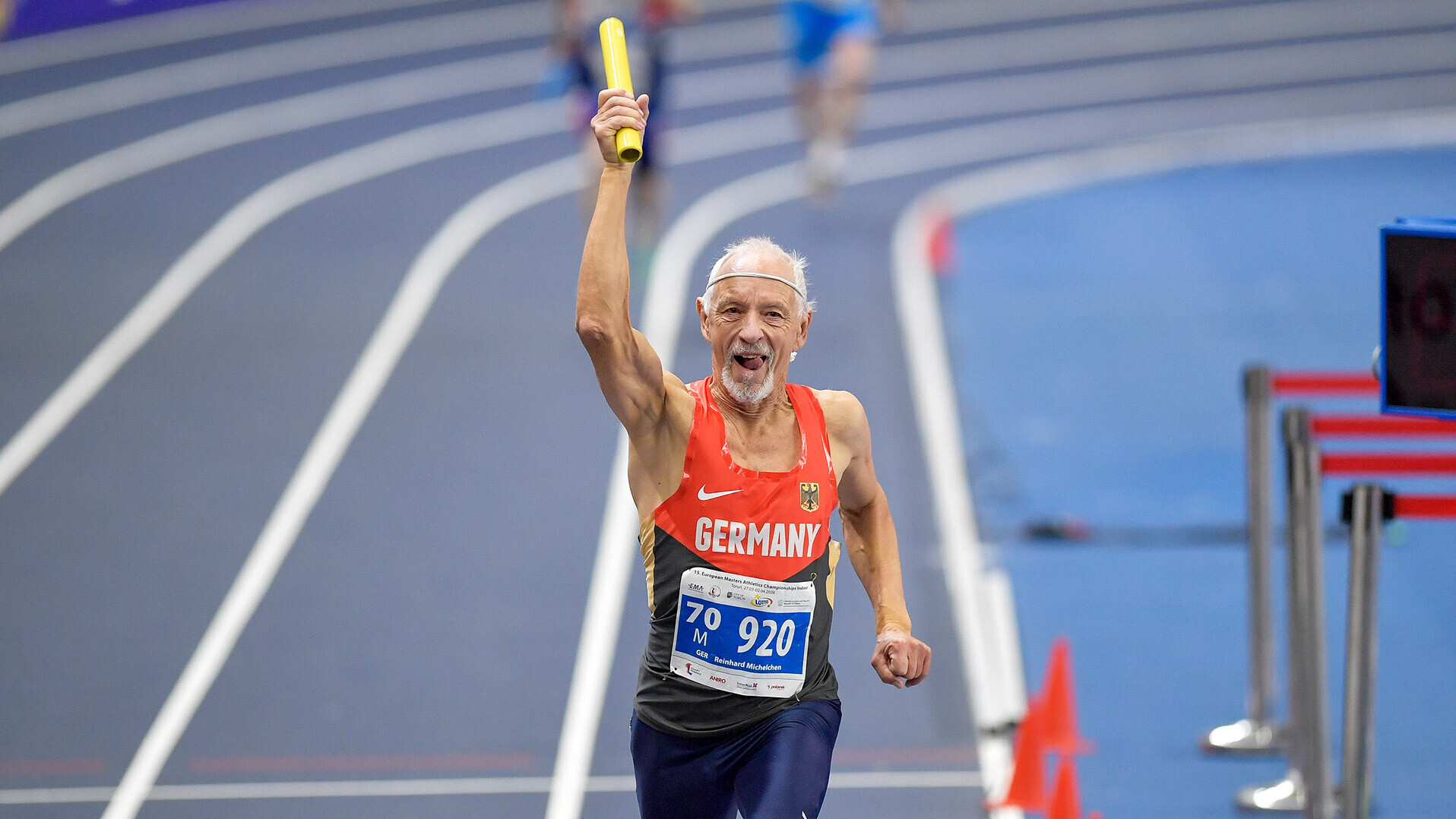 Reinhard Michelchen läuft über die Ziellinie und reckt den rechten Arm mit dem Staffelstab in die Luft