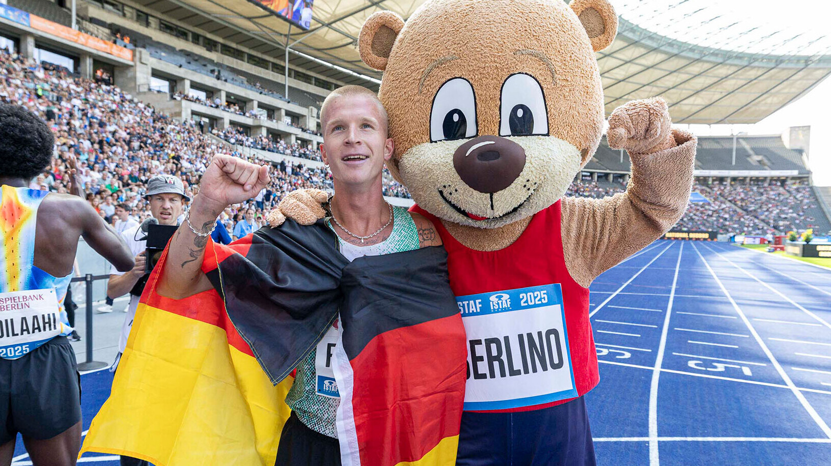 Robert Farken mit Deutschlandfahne um den Schultern neben dem Maskottchen Berlino