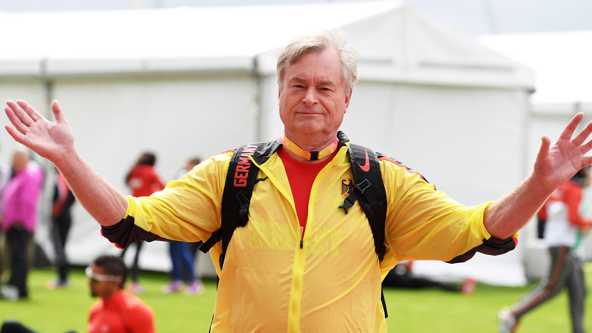 Hartmut Grothkopp mit ausgebreiteten Armen in gelber Nationalmannschaftsjacke