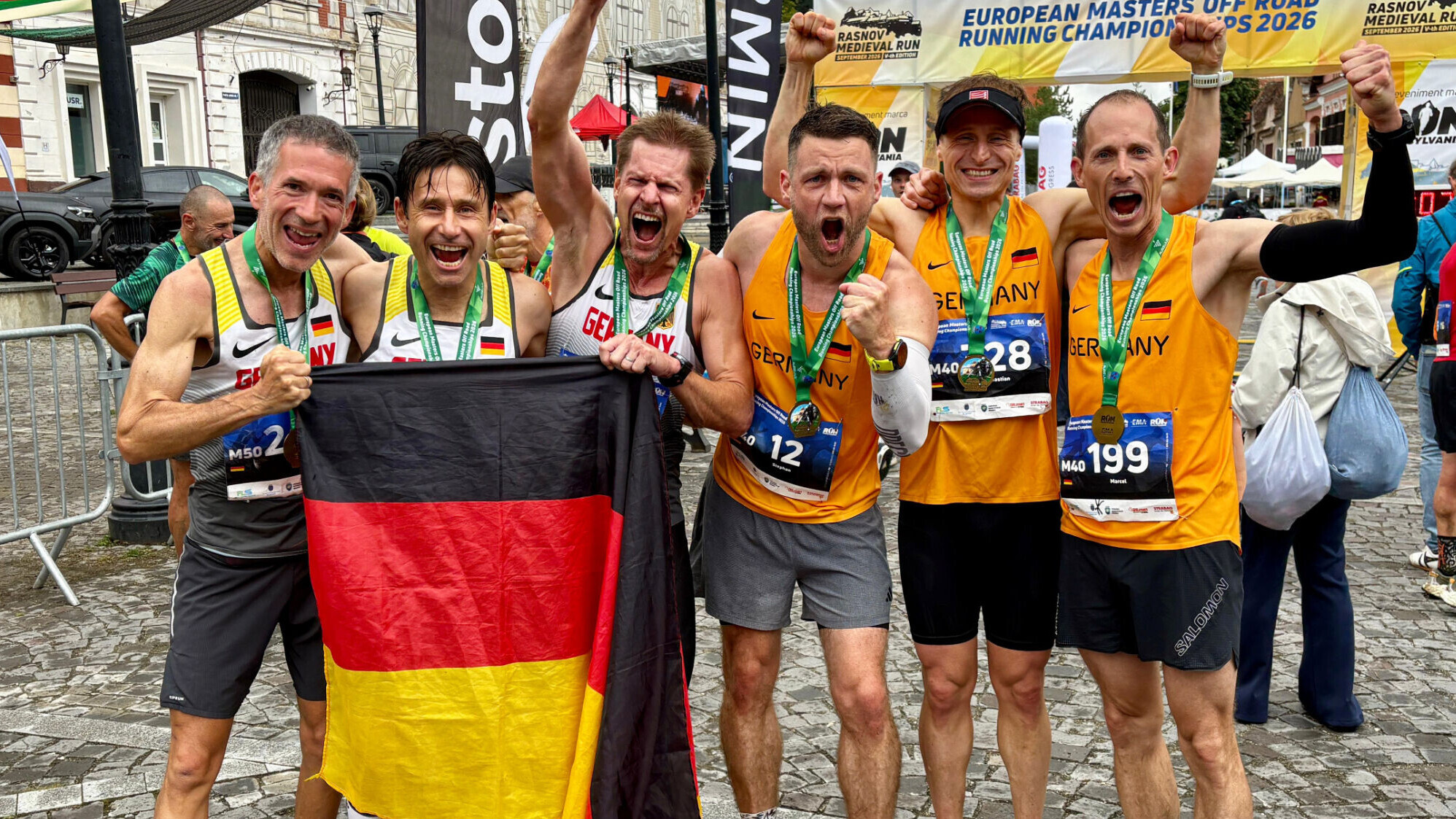 Sechs deutsche Masters-Athleten jubeln im Nationaltrikot und einer Deutschlandfahne in die Kamera.