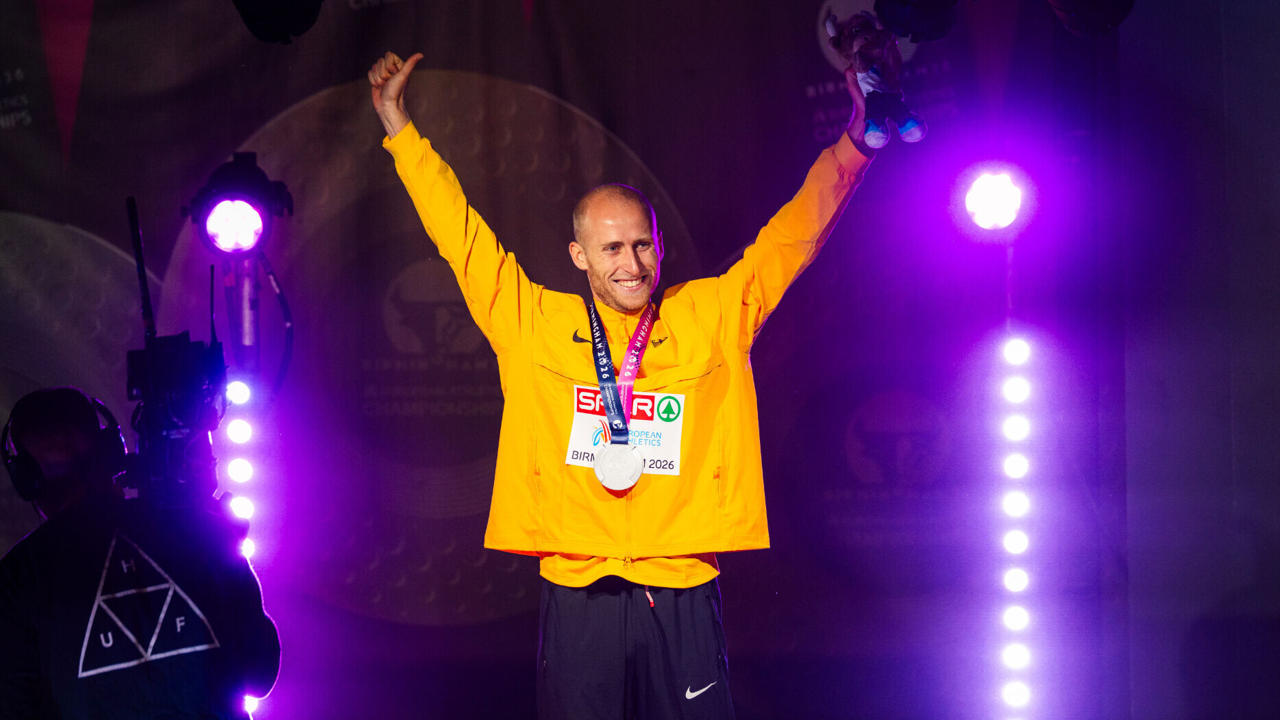 Der deutsche Läufer Florian Bremm streckt jubelnd bei einer Sigerehrung beide Arme in die Höhe und hat dabei eine Silbermedaille um den Hals.