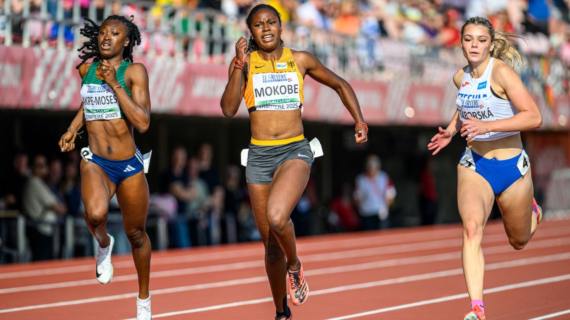 Judith Mokobe sprintet im Deutschland-Trikot mit der Startnummer „Tampere 2025“ zwischen zwei Konkurrentinnen auf einer roten Bahn, angestrengt und mit geballten Fäusten.