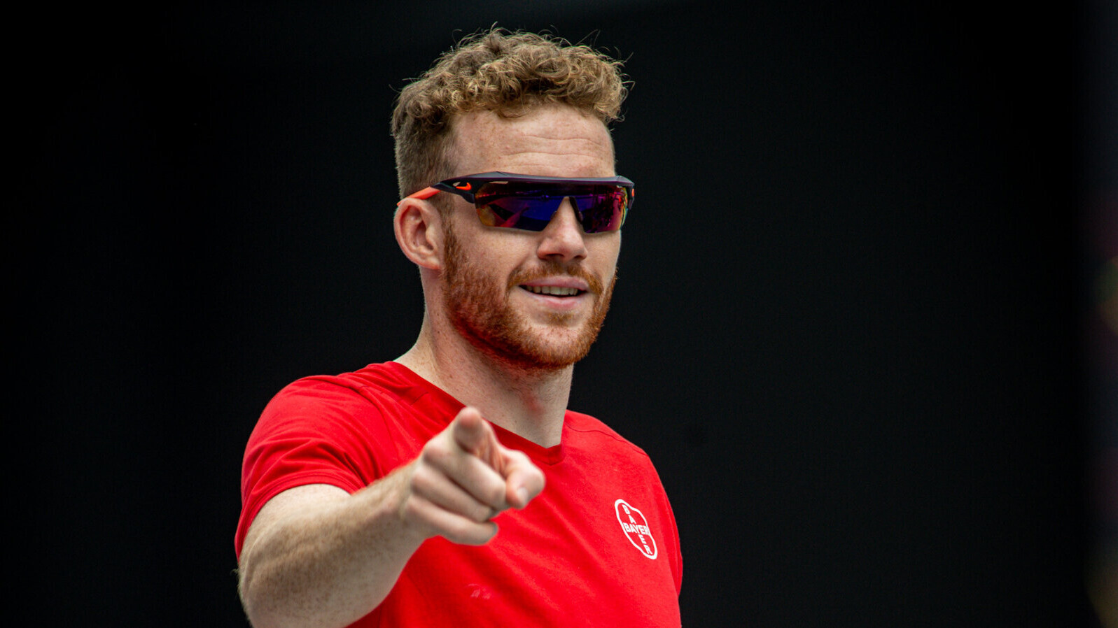 Stabhochspringer Torben Blech, im roten Bayer-Leverkusen-Shirt und mit Sonnenbrille, streckt in einer Jubelgeste den rechten Zeigefinger nach vorn. 