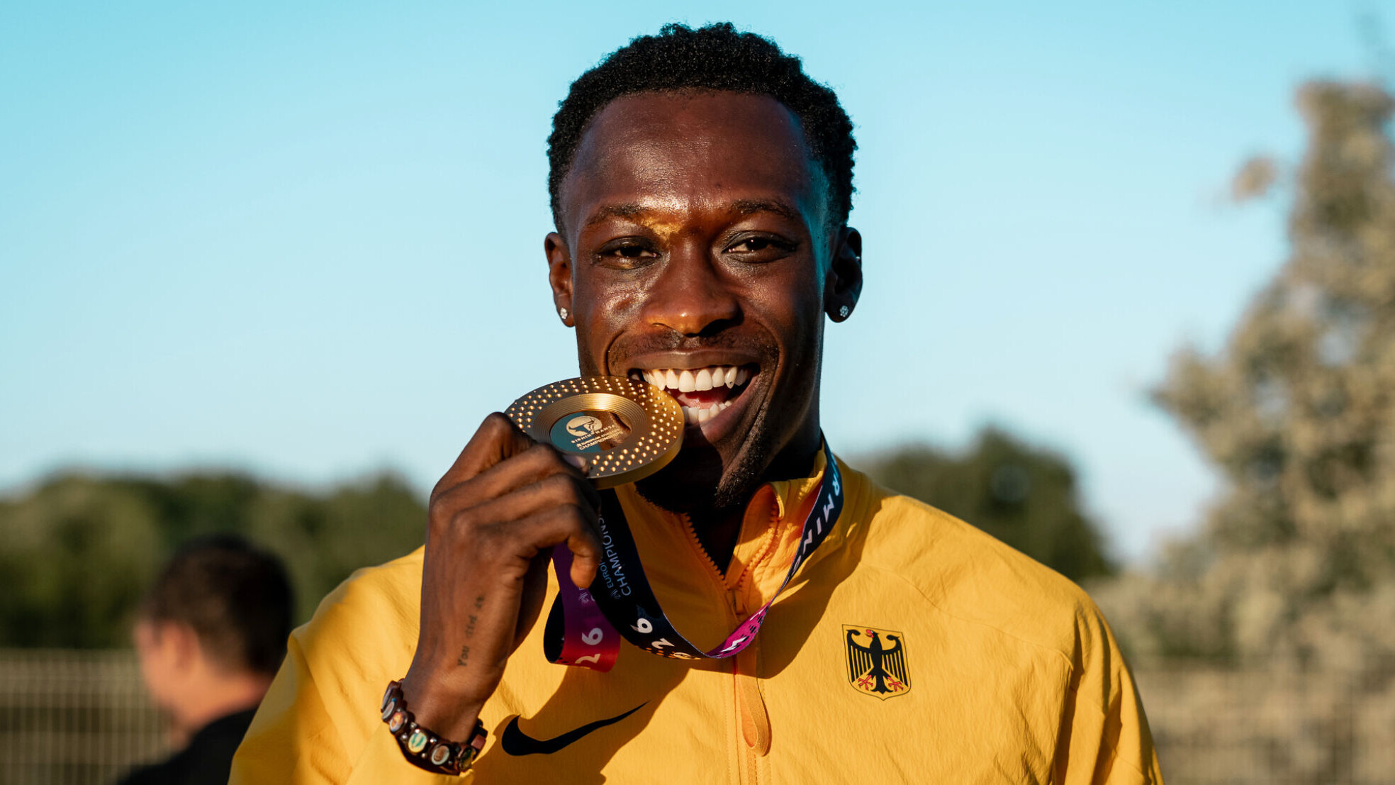 Portrait des deutschen Sprinters Owen Ansah. Er trägt eine Goldmedaille um den Hals und deutet an, in diese hineinzubeißen.