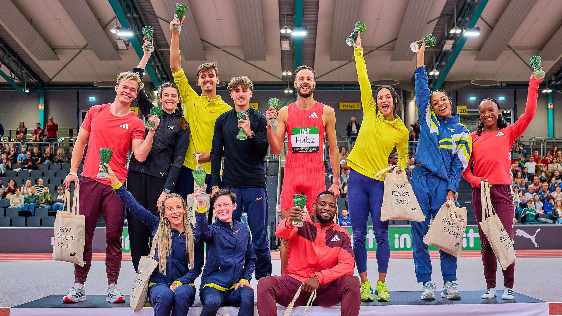 Eine Reihe von Leichtathleten stehen und sitzen auf einem Podest und strecken Pokale in die Höhe.