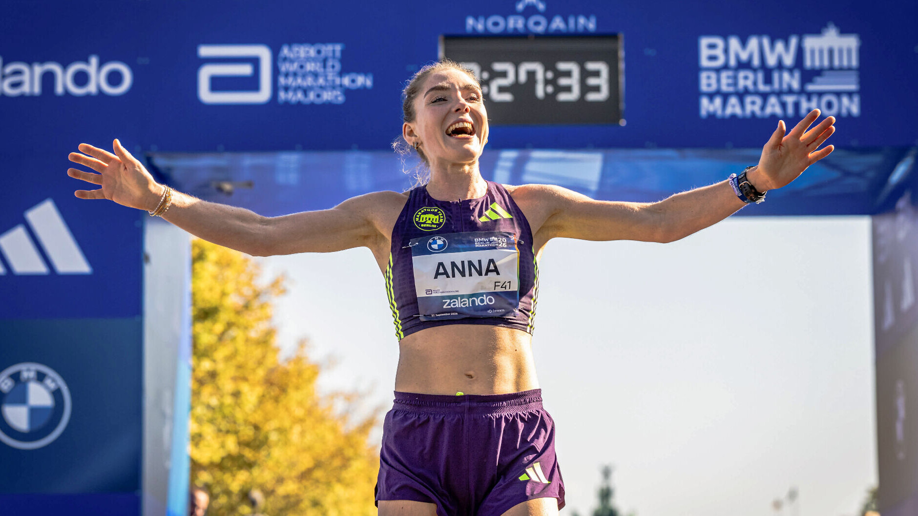 Die deutsche Läuferin jubelt im Zielbereich des Berlin-Marathon 2026. Dabei lacht sie und breitet die Arme aus.