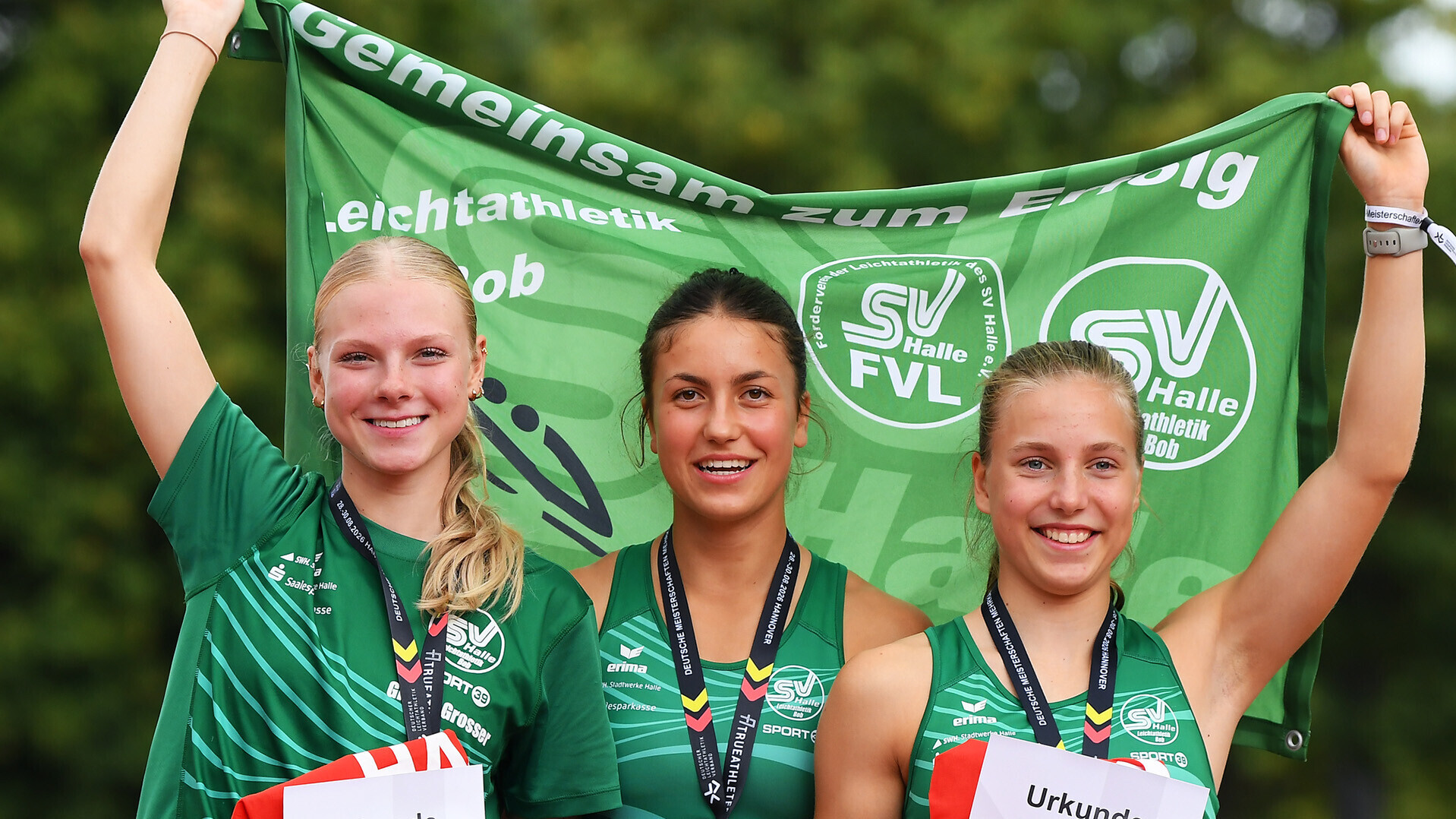 Gisele Grosser, Julia Malcharek und Annabell Flizikowski halten Urkunden in der Hand und eine Fahne des SV Halle in die Höhe