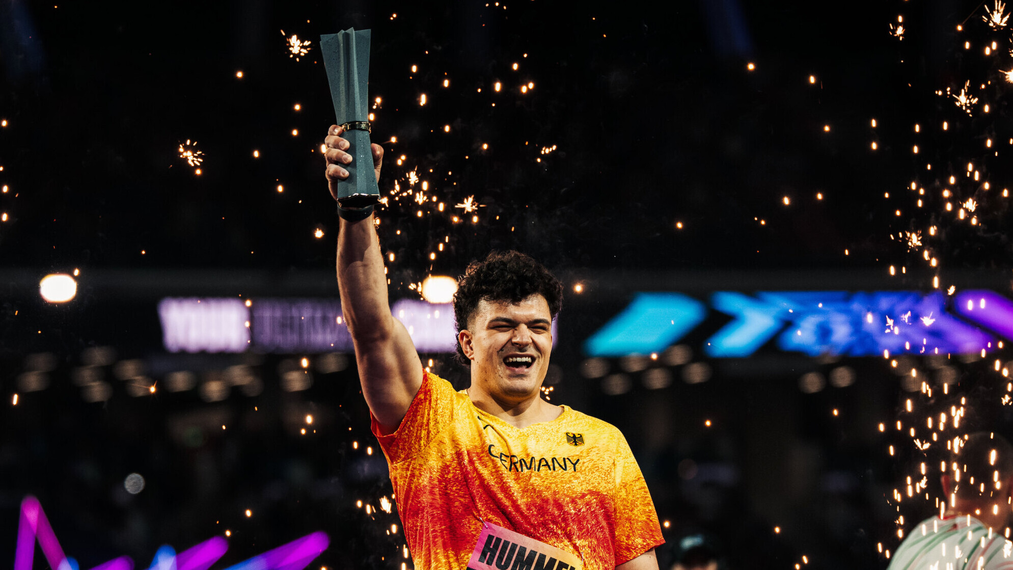Der deutsche Hammerwerfer Merlin Hummel streckt mit der rechten Hand die Trophäe der World Athletics Ultimate Championships in die Höhe.