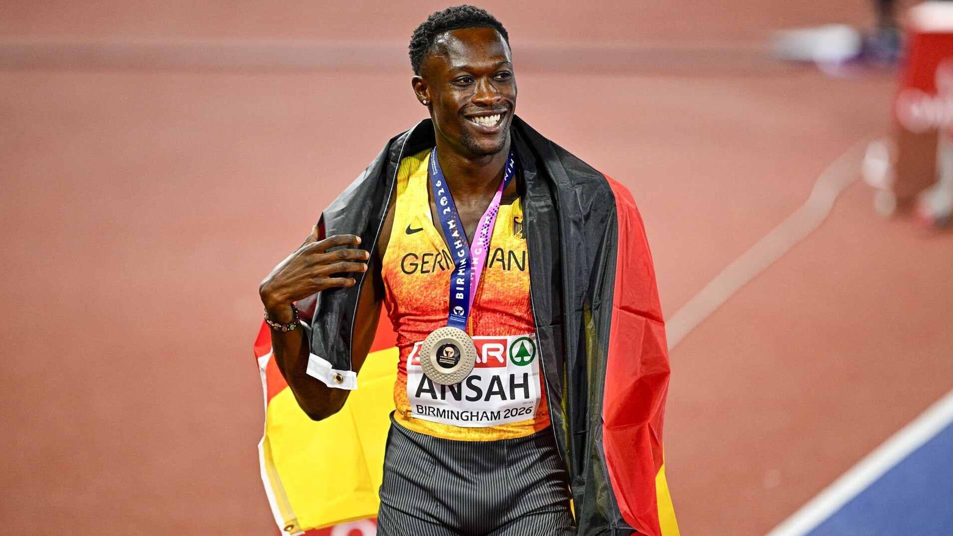 Sprinter Owen Ansh mit der Bronzemedaille und der Deutschland-Fahne um dem Hals.