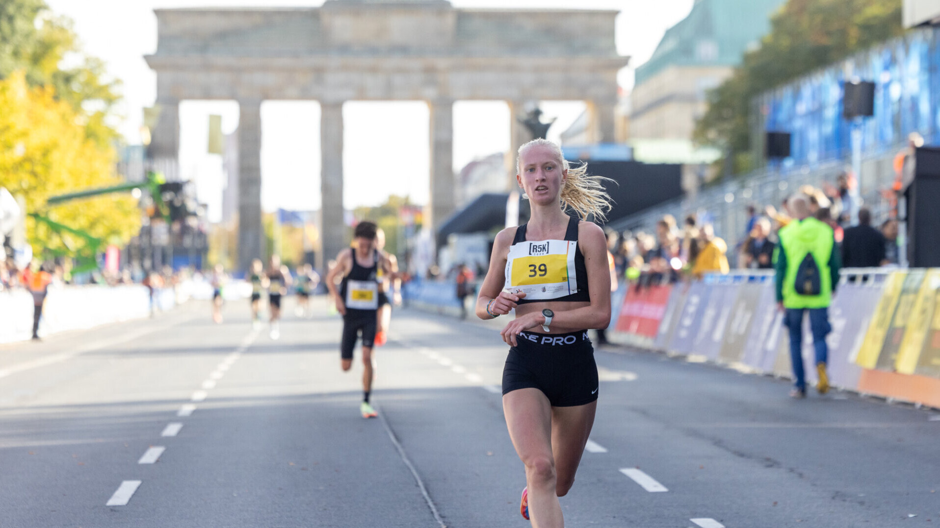 Carolina Schäfer läuft mit einem Blick auf die Uhr beim Straßenlauf ins Ziel, im Hintergrund ist das Brandenburger Tor zu sehen. 
