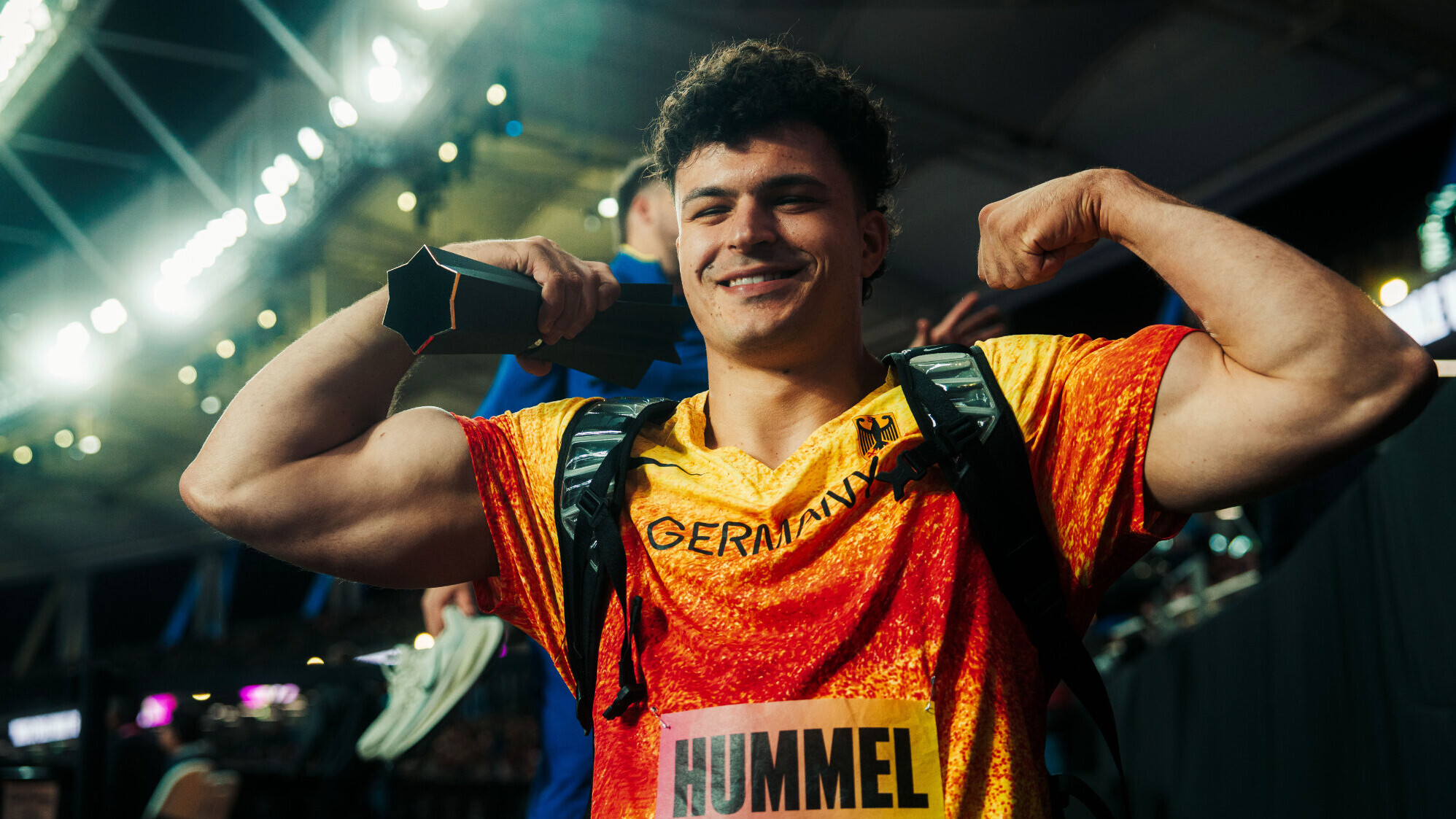 Der deutsche Hammerwerfer Merlin Hummel im Nationaltrikot hebt die Arme zur Seite, beugt den Ellenbogen und spannt die Oberarmmuskeln an.