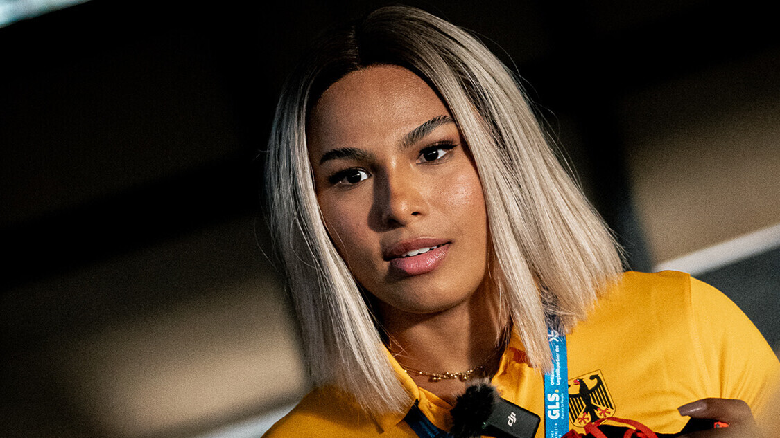 Porträt der deutschen Weitspringerin Laura Raquel Müller mit einem gelben Nationalmannschaftsshirt und mit einem Sportschuh in der Hand