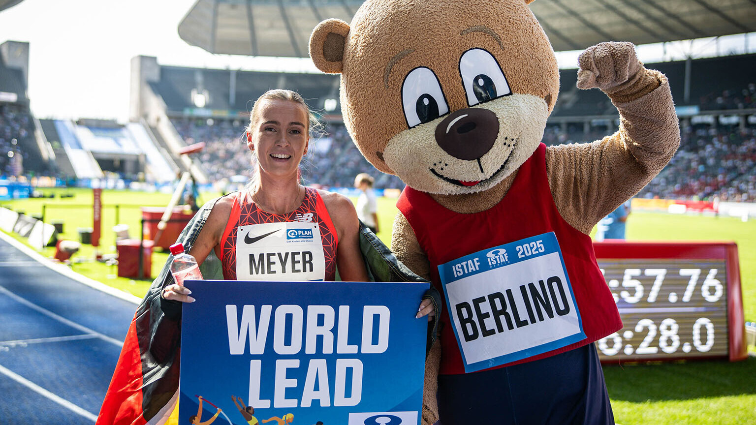 Lea Meyer mit einem Schild "World Lead" in der Hand und einer Deutschlandfahne um die Schultern neben dem Maskottchen Berlino