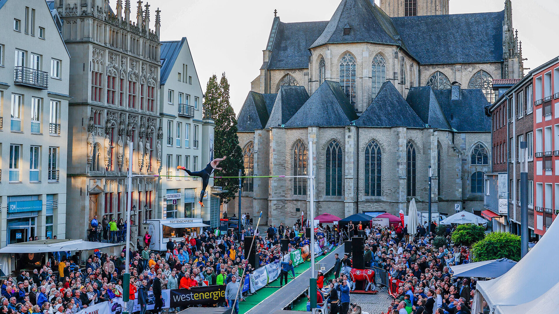 Die Stabhochsprunganlage auf dem Domplatz von Wesel, ein Athlet schwingt sich gerade über die Latte. Im Hintergrund das Publikum sowie der Dom