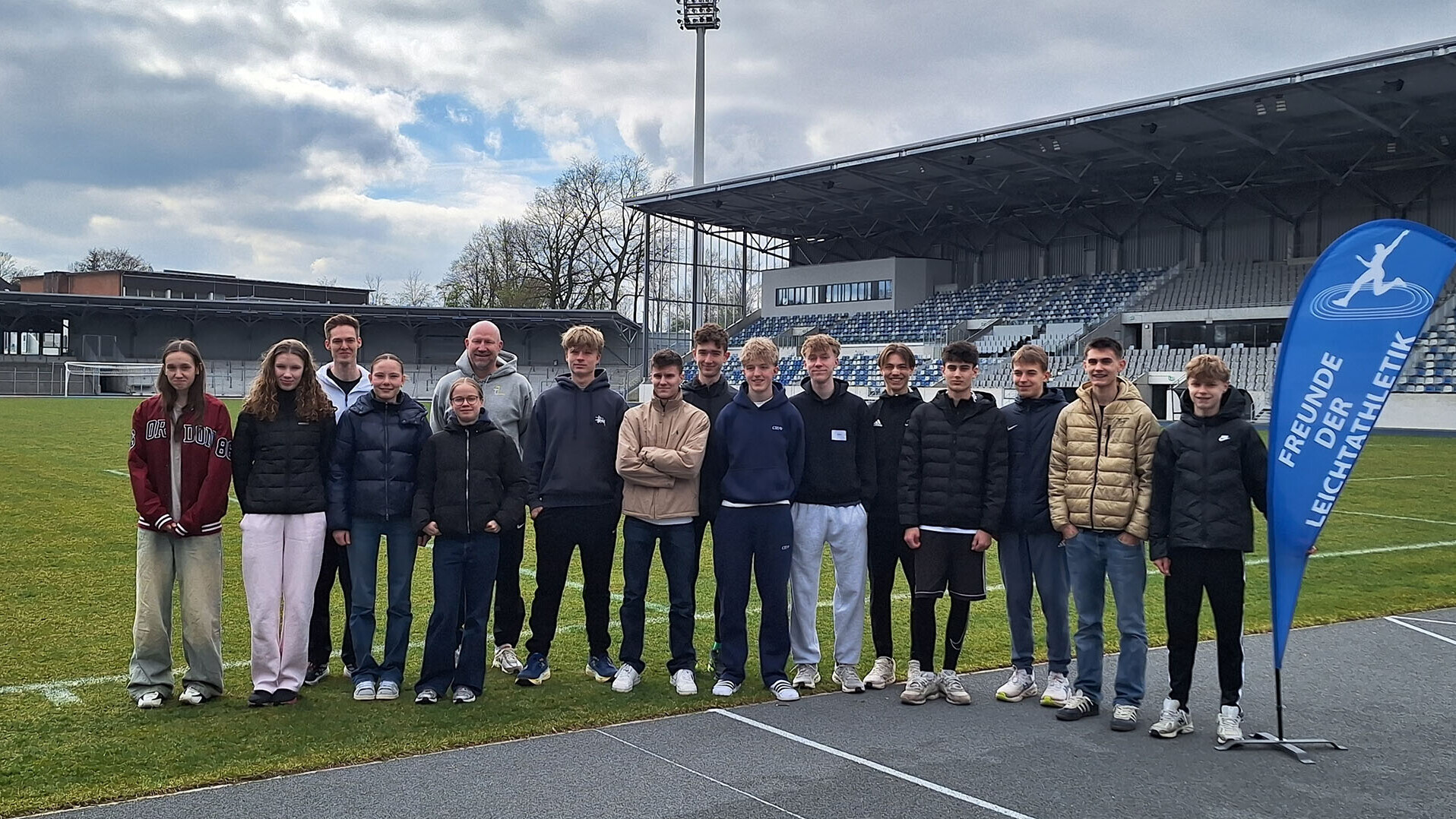 Eine Gruppe von Personen auf dem Rasen in einem Stadion, neben der Gruppe ein Banner mit der Aufschrift "Freunde der Leichtathletik"