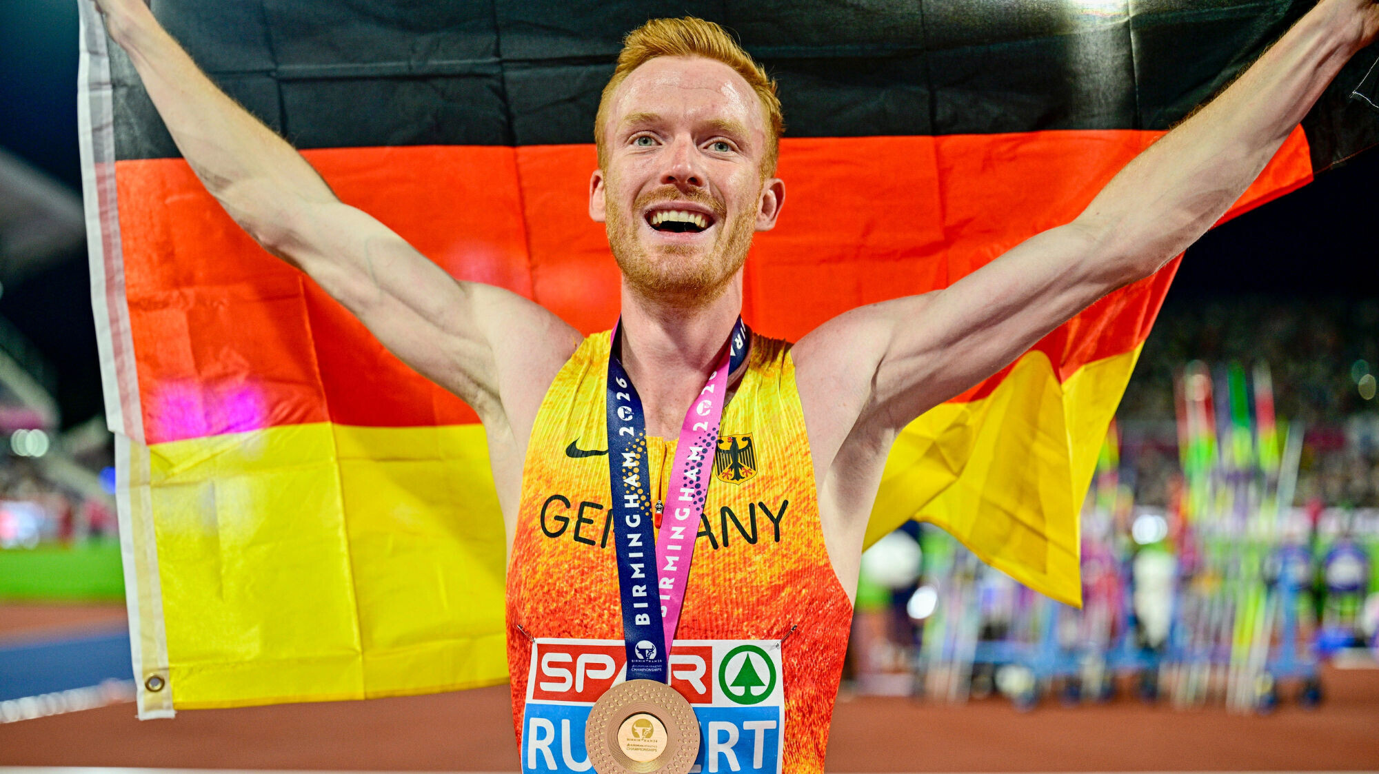 Der deutsche Hindernislaufer hält eine Deutschlandfahne in die Höhe und hat dabei eine Goldmedaille um den Hals.