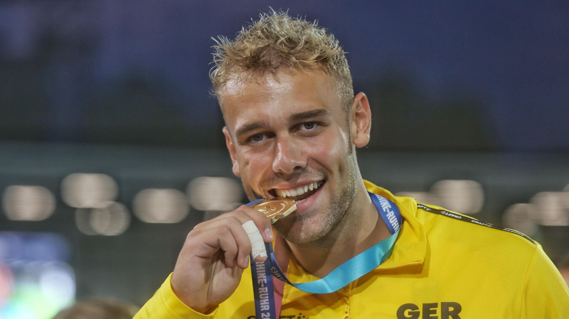 Diskuswerfer Mika Sosna beißt in seine Goldmedaille.