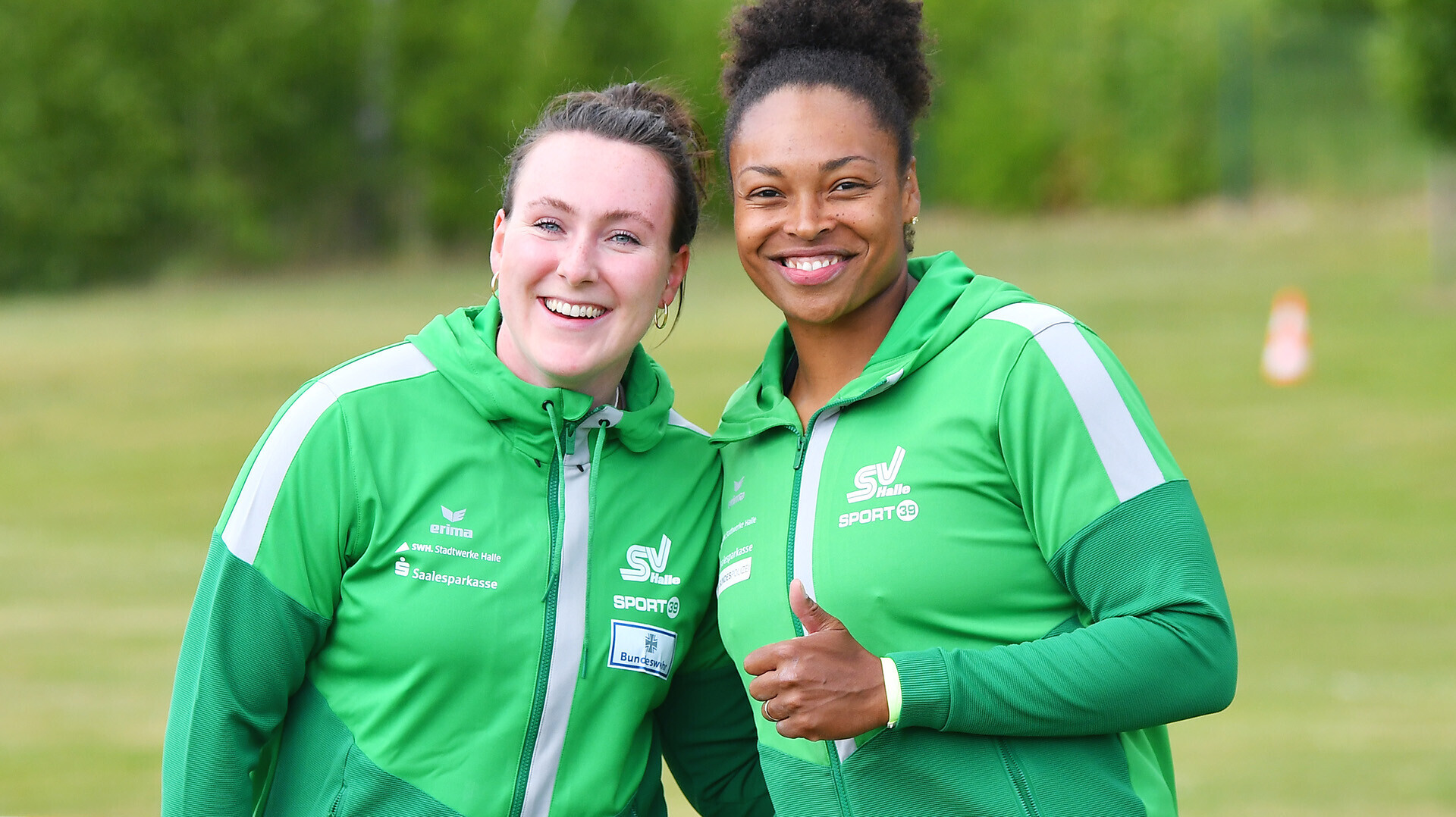 Die Diskuswerferinnen Antonia Kinzel und Shanice Craft, beide im grünen Trikot des SV Halle, posieren für ein Foto, Shanice Craft reckt den linken Daumen nach oben. 