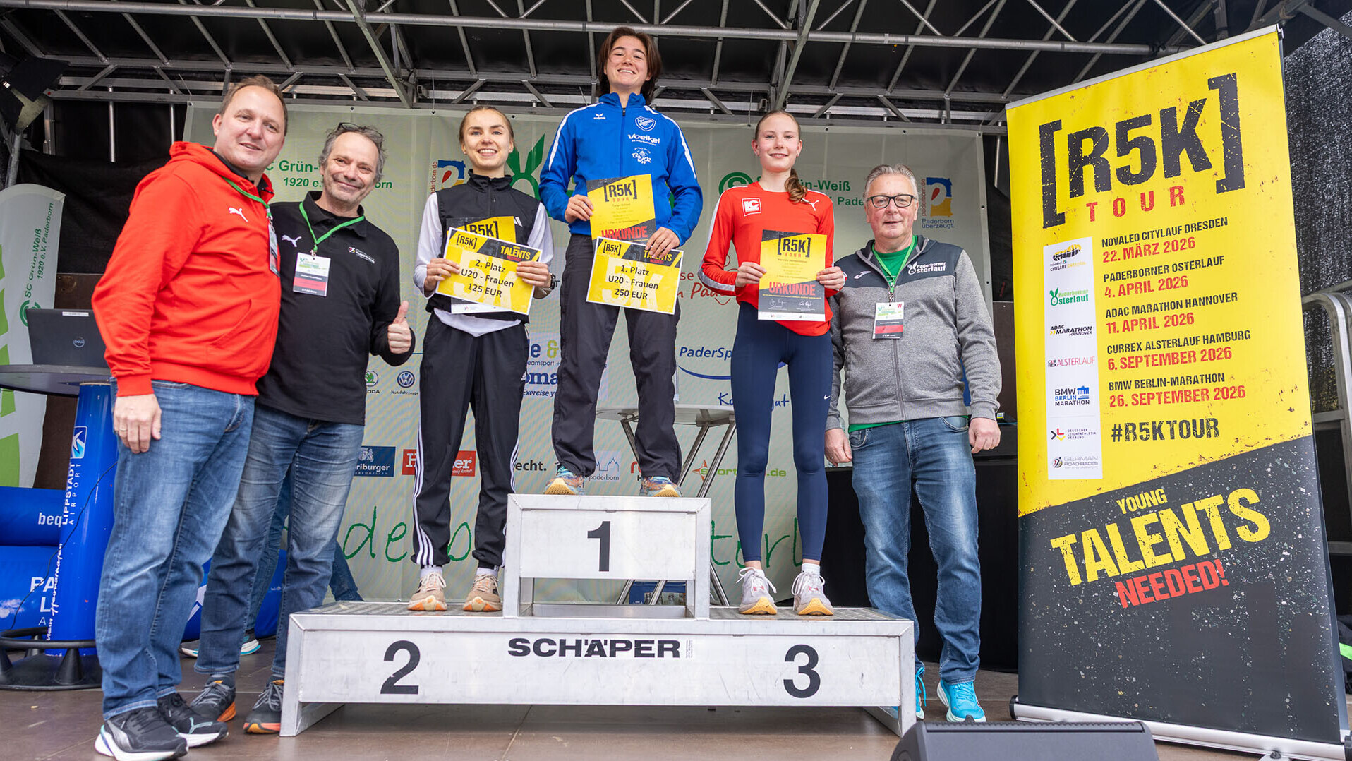 Ein Podium mit drei Athletinnen und einem Banner mit der Aufschrift R5K und Wettkampfterminen