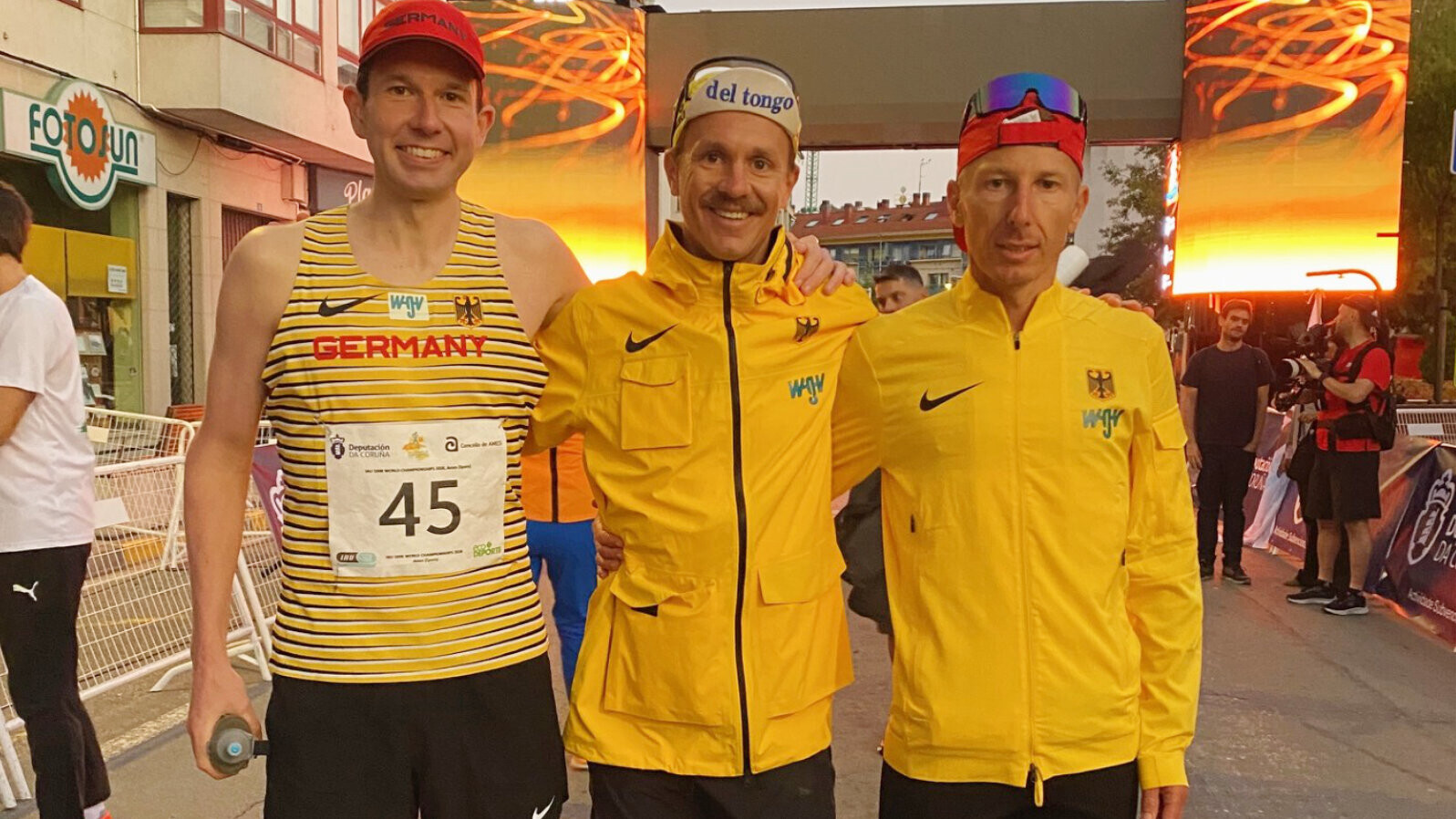 Die deutschen Ultraläufer Martin Müller, Felix Weber und Stephan Fruhmann stehen im Nationaldress Arm in Arm nebeneinander.
