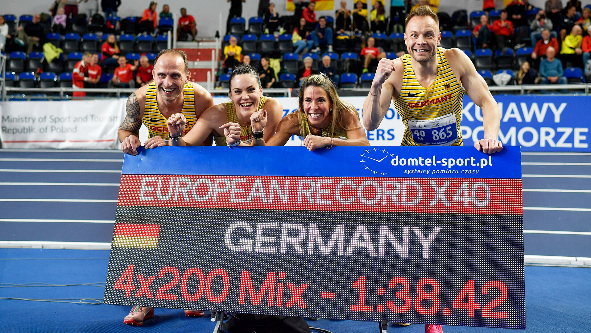 Zwei Männer und zwei Frauen posieren vor einer Anzeigetafel mit der Aufschrift "European Record X40, Germany, 4x200 Mix,1:38,42"