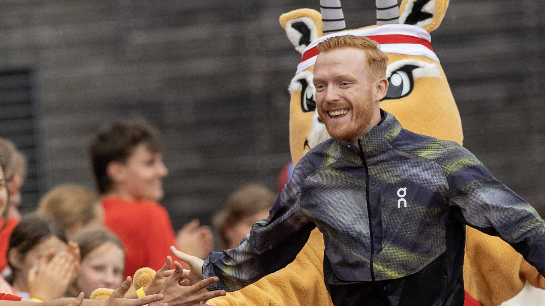 Frederik Ruppert klatscht bei der Athletenpräsentation Kinder ab, im Hintergrund das Maskottchen. 