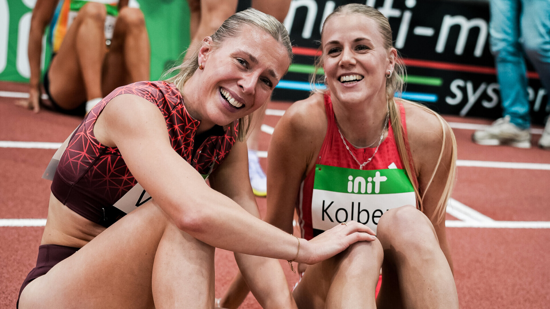 Die deutschen Läuferinnen Nele Weßel und Majtie Kolberg sitzen nebeneinander auf der Laufbahn und lächeln.