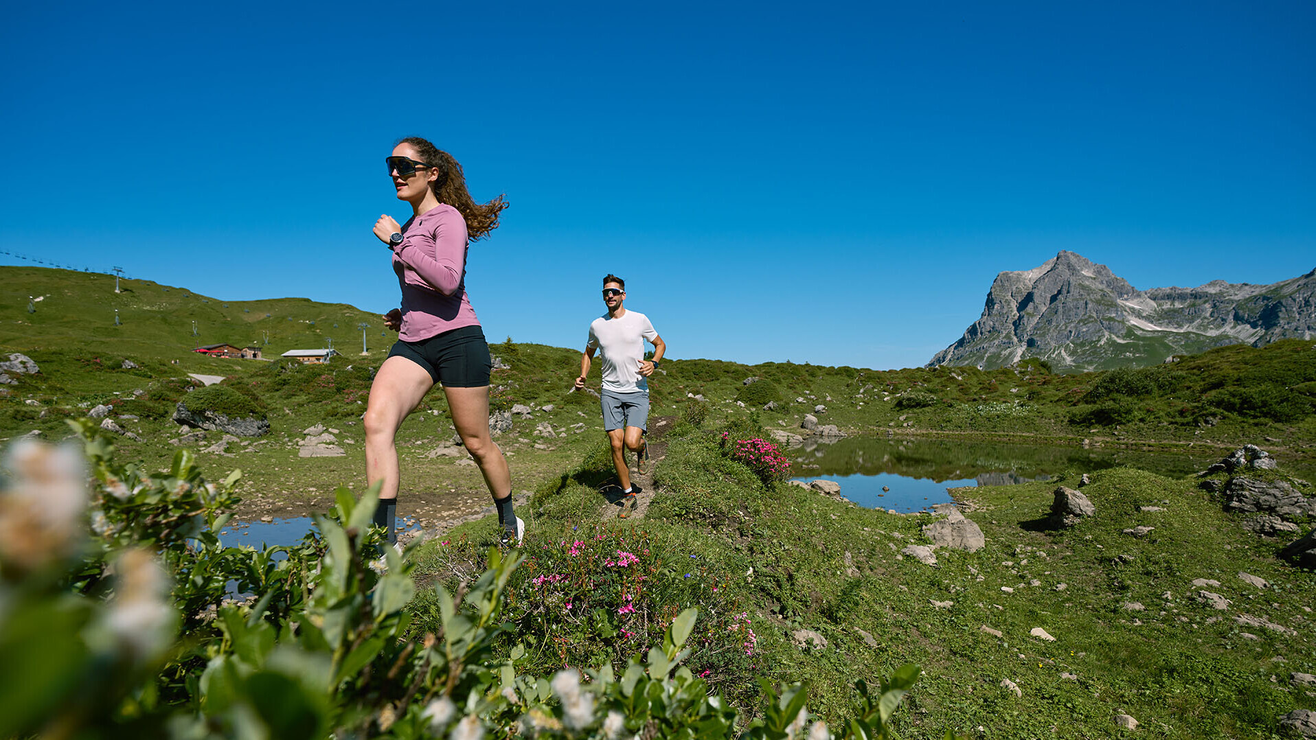 Ein Mann und eine Frau absolvieren auf dem grünen Untergrund in Warth-Schröcken einen Traillauf. 