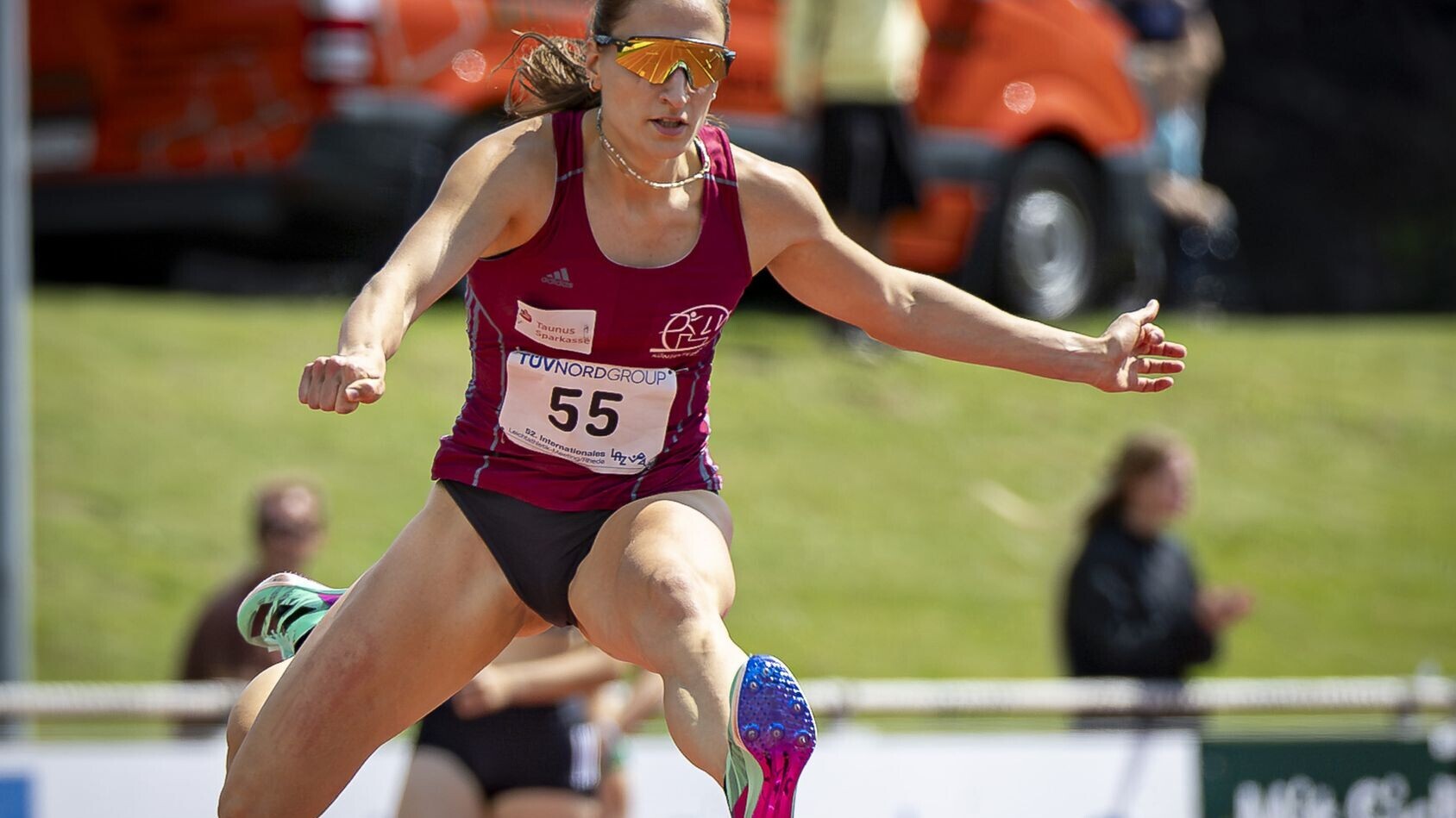 Elena Kelety im roten Vereinstrikot mit Sonnenbrille beim Überqueren einer Hürde. 