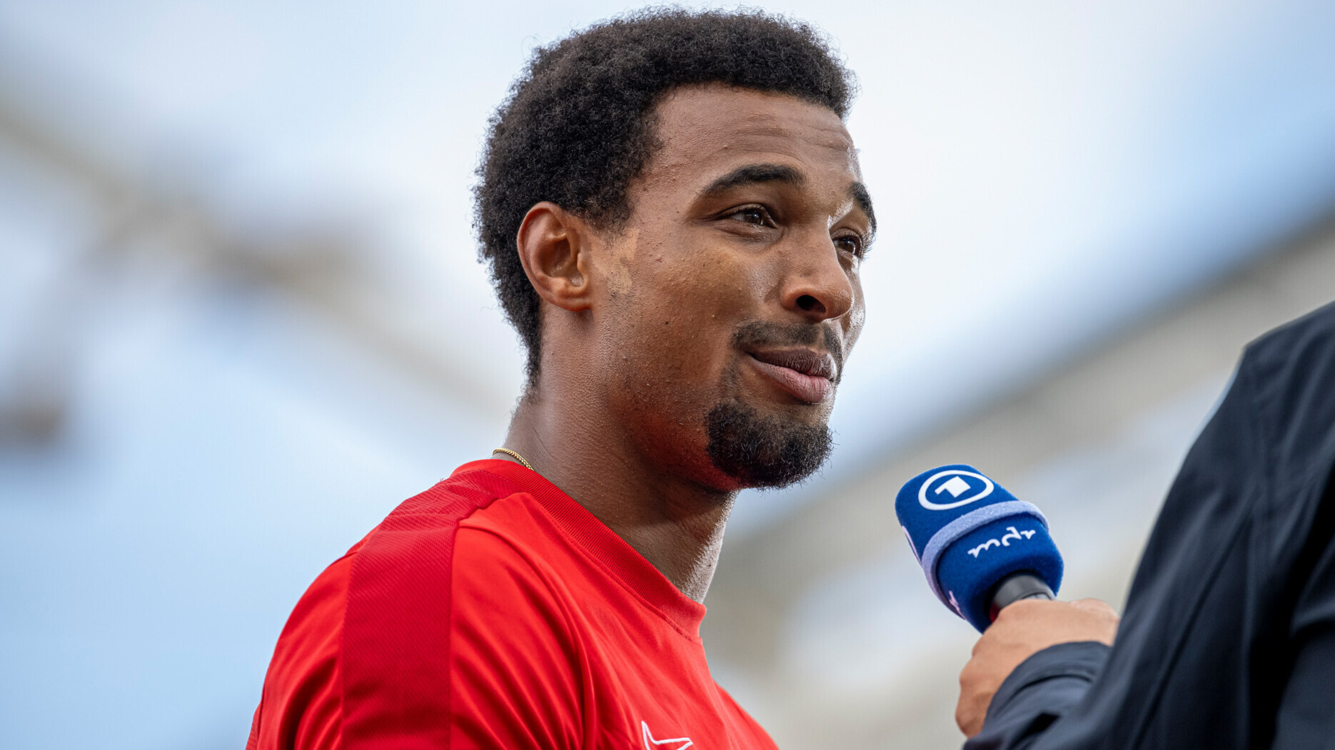 Leo Neugebauer im roten Shirt, eine Hand hält ihm ein Mikrofon vor das Gesicht