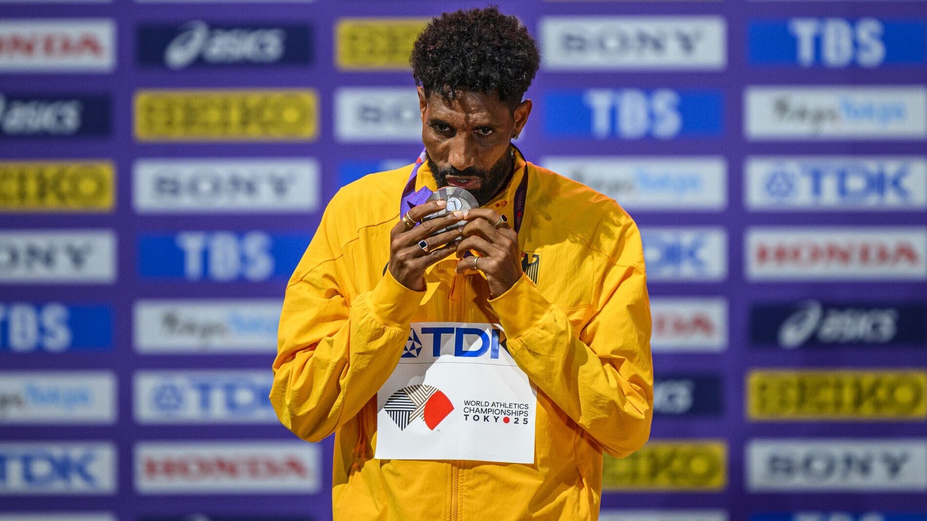 Amanal Petros, im gelben Nationalmannschaftsoutfit, küsst auf dem Podium seine WM-Medaille