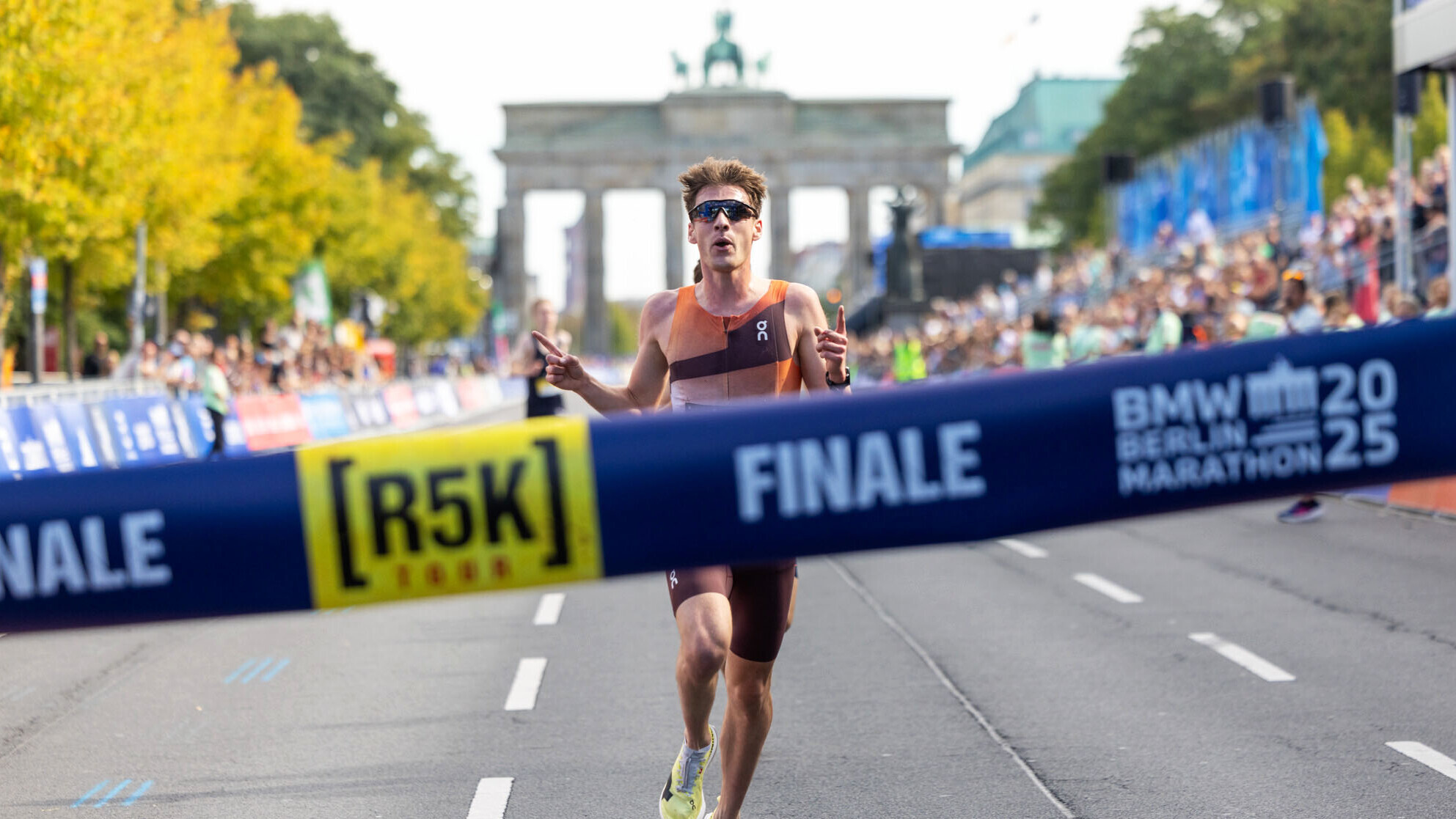 Christoph Schrick nähert sich mit einer Jubelgeste dem Zielband mit der Aufschrift "R5K-Finale", im Hintergrund das Brandenburger Tor