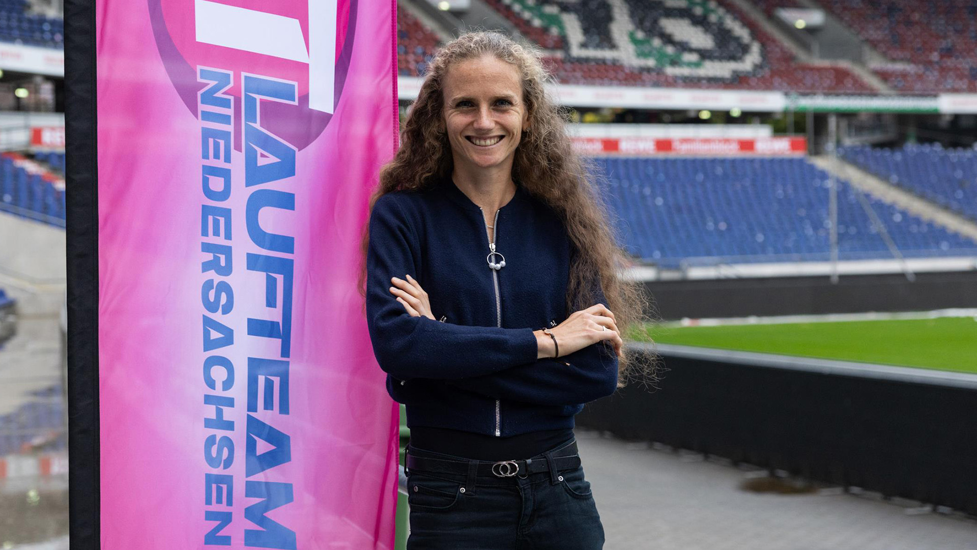 Fabienne Königstein im Stadion von Hannover 96 neben einem rosafarbenen Banner, auf dem "Laufteam Niedersachsen" steht