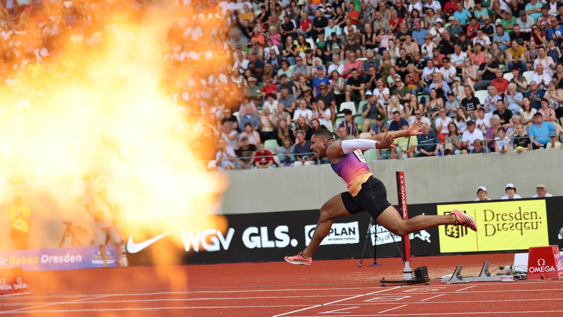 Hürdensprinter Gregory Minoué wirft sich ins Ziel, links eine Feuerfontäne. 