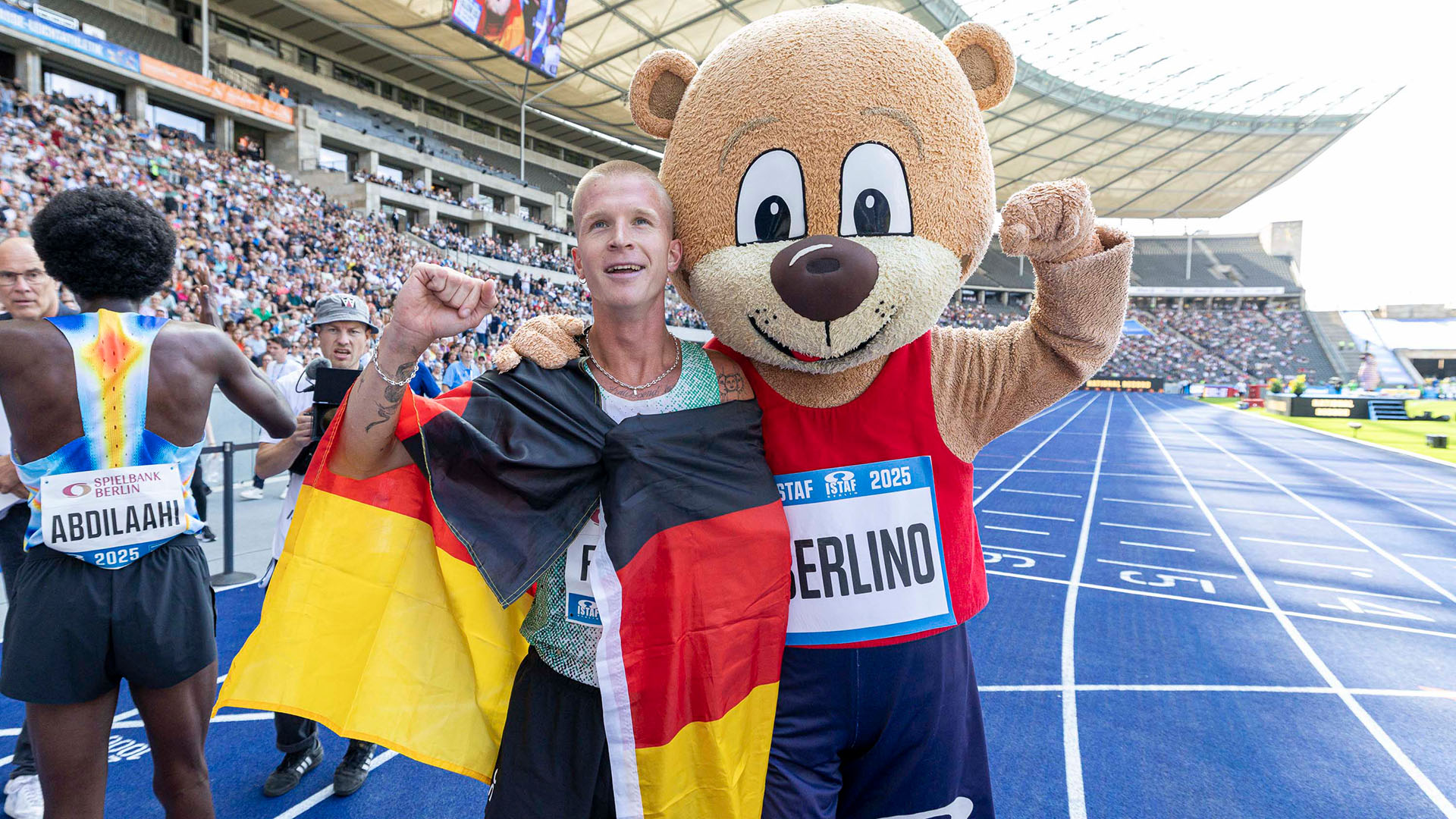 Robert Farken mit Deutschlandfahne um den Schultern neben dem Maskottchen Berlino